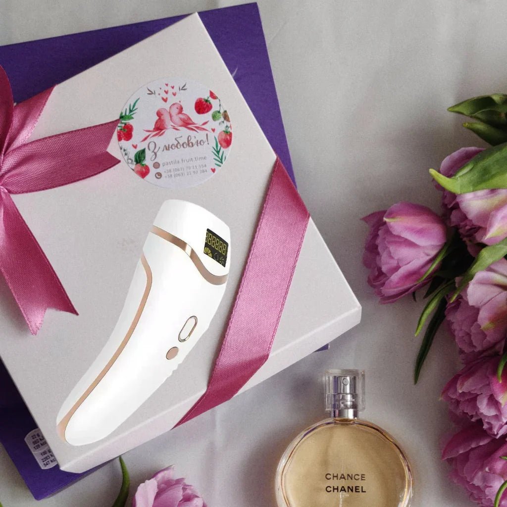 White IPL hair removal device with pink ribbon, Chanel perfume bottle, and pink flowers on a white background
