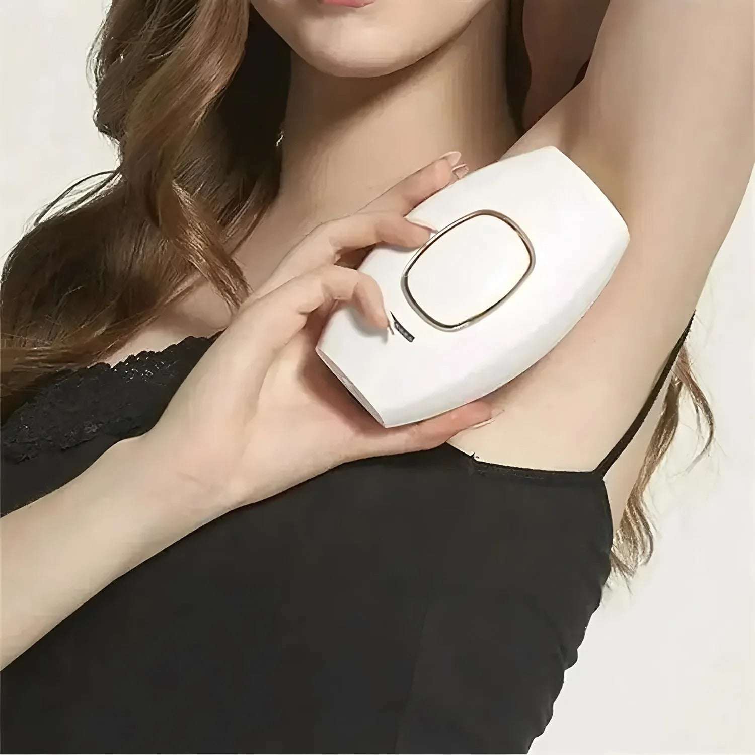 Woman using a white IPL hair care device on her underarm with a plain background