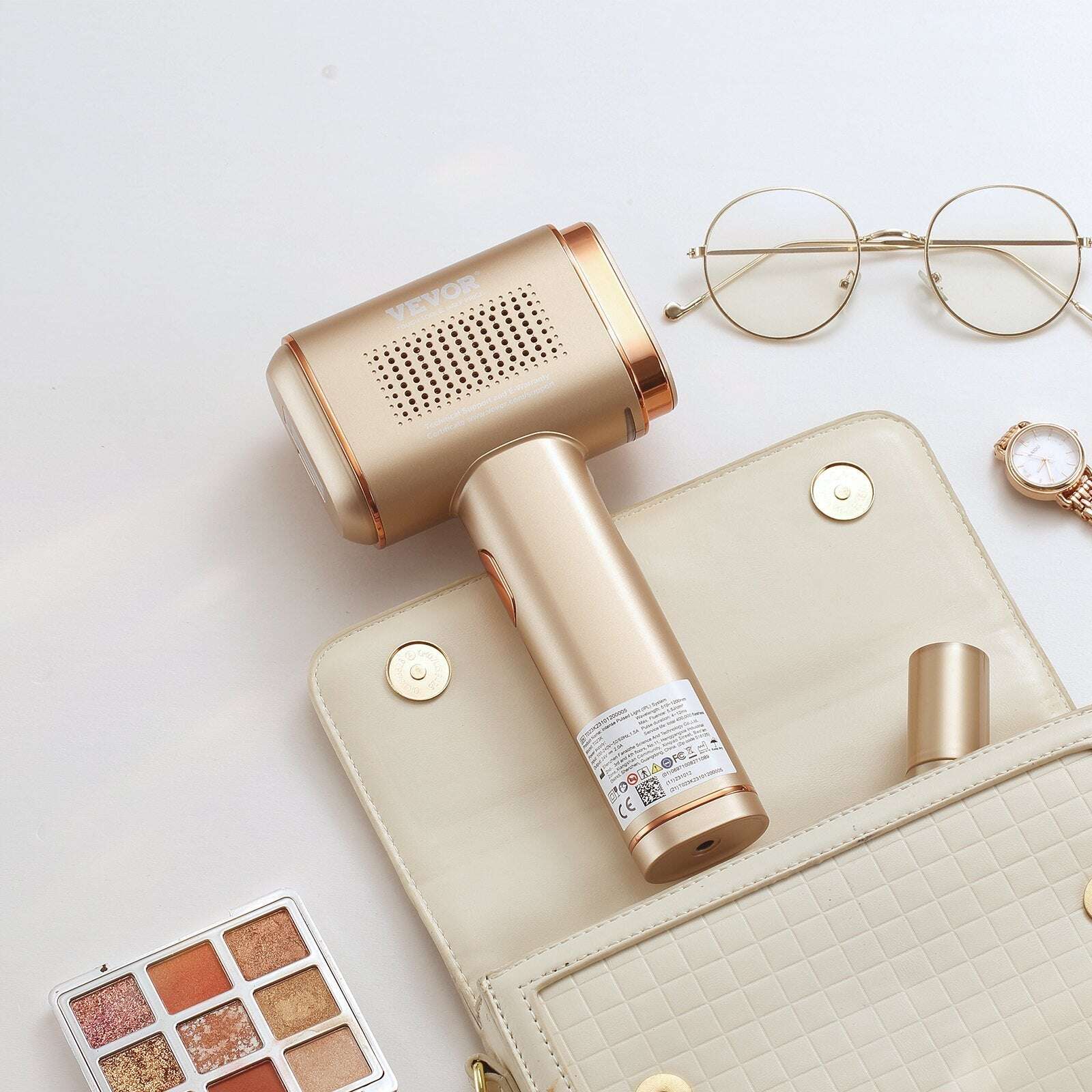 Gold IPL Hair reduction device on a light surface with a handbag, eyeglasses, and makeup palette.